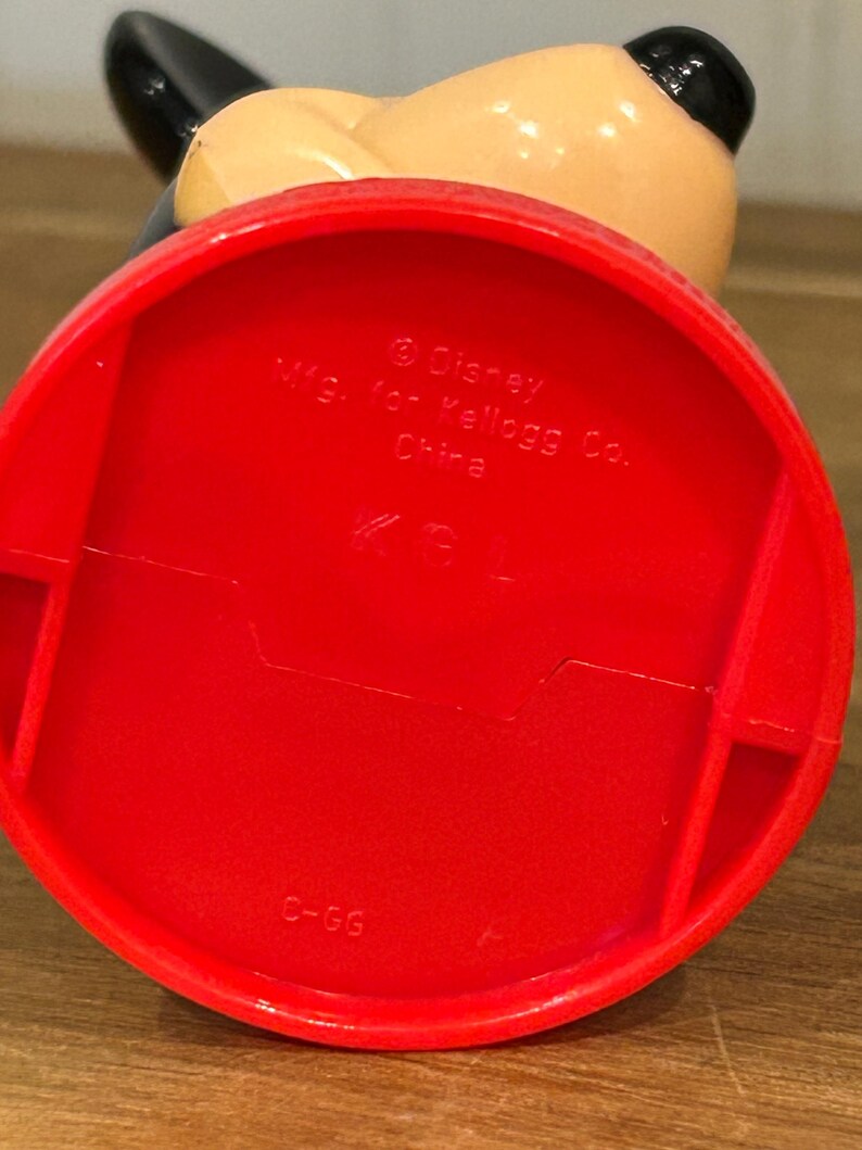 May include: A red plastic Mickey Mouse figurine base with the text "&copy; Disney Mfg. for Kellogg Co. China". The figurine has a black ear and a tan head.