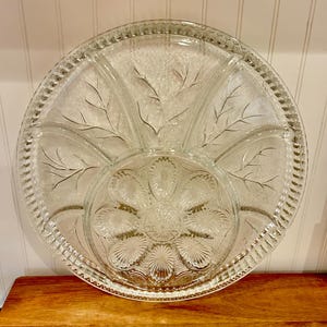 Op de afbeelding: Een glazen serveerschaal met een gegolfde rand en een bloemmotief. De schaal heeft zes afzonderlijke secties en een centrale sectie.