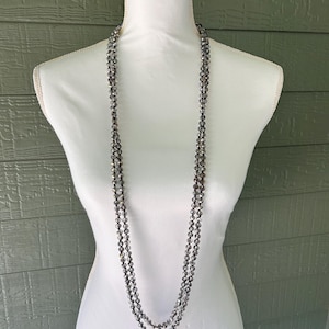 May include: A long, double-strand necklace featuring faceted, translucent grey beads. The beads are strung on a thin cord, creating a continuous loop that hangs down in two distinct layers against the white display form.