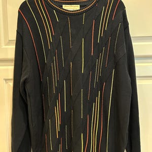 May include: Black sweater with vertical stripes in yellow, orange, and red. The sweater has a ribbed collar, cuffs, and hem with orange trim. The brand name "Harve Thompson" is visible on the collar.