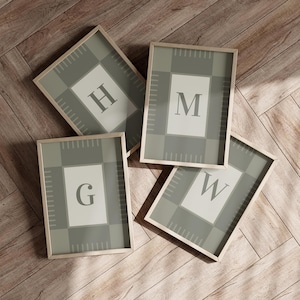 May include: Four framed art prints with the letters G, H, M, and W. Each print features a light green and gray plaid pattern with a white central rectangle containing a single letter. The frames are light wood.