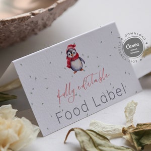 Op de afbeelding: Een wit voedseletiket met een pinguïn die een rode muts en sjaal draagt. Het etiket zegt "volledig bewerkbaar Voedseletiket" en heeft een grijze achtergrond met kleine groene stippen.