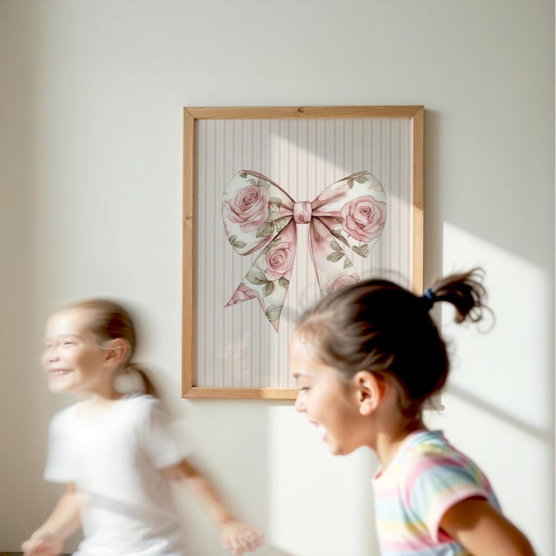 May include: A framed print featuring a watercolor illustration of a bow adorned with roses. The bow is in shades of pink and white, set against a striped background. The frame is made of light-colored wood.