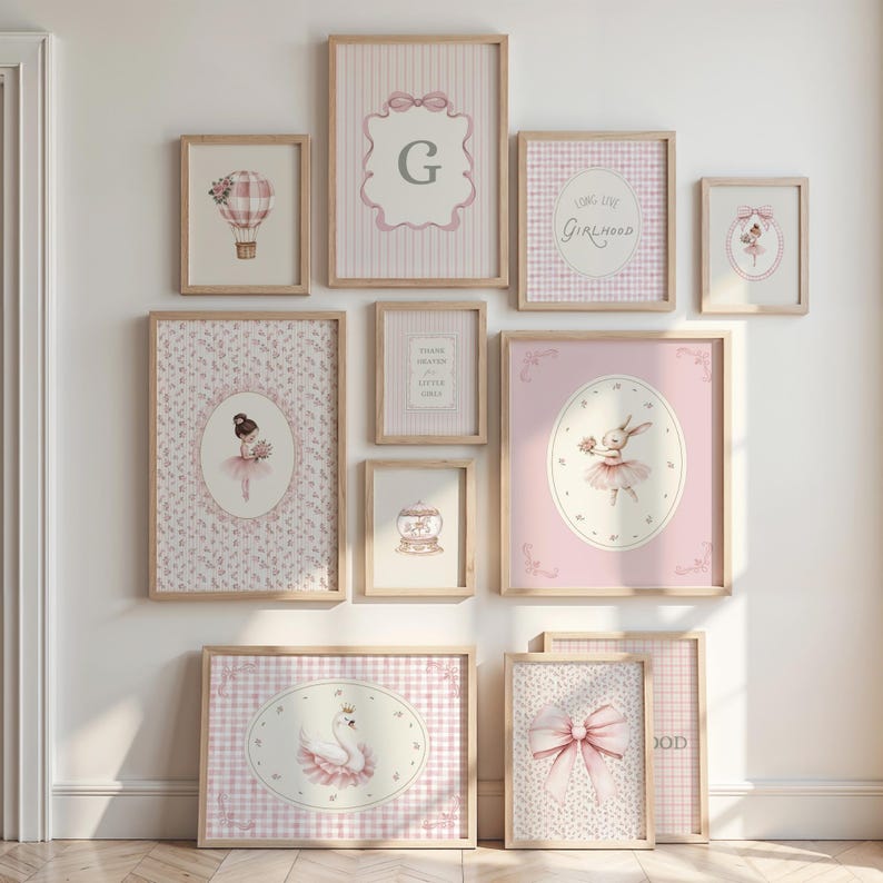 May include: A collection of framed art prints in a nursery theme. The prints feature illustrations of a hot air balloon, a ballerina, a swan, and a bunny, all in soft pink and white tones. Some prints include text, and all are in wooden frames.