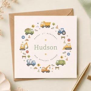 May include: A square greeting card featuring a circular arrangement of watercolor construction vehicles, traffic cones, and road signs. The center text reads "Happy 1st Birthday", "Hudson", and "Our Special Nephew" in a simple font.