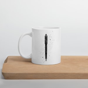 Puede incluir: Taza de cerámica blanca con una ilustración en blanco y negro de una pluma estilográfica sobre un fondo blanco.