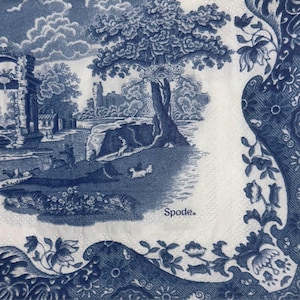May include: A blue and white Spode napkin featuring a pastoral landscape scene with trees, buildings, and figures. The design includes a decorative border with floral and scroll elements. The word "Spode" is printed on the napkin.