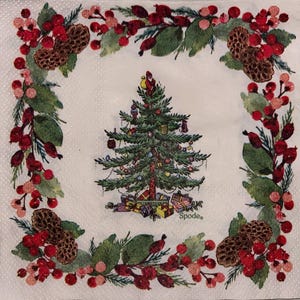 May include: A white square napkin with a Christmas theme. The center features a decorated Christmas tree with presents. The border has a garland of red berries, green leaves, and pinecones. The Spode logo is visible.