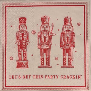 May include: A white square paper napkin with a red border and three red nutcracker illustrations. The text "LET'S GET THIS PARTY CRACKIN'" is printed at the bottom. The napkin has a dotted border and snowflake accents.