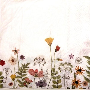 May include: A square paper napkin featuring a white background with a colorful botanical print along the bottom edge. The design includes various wildflowers, ferns, and grasses in shades of yellow, red, pink, purple, and green.