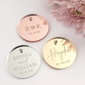 May include: Three round, mirrored acrylic tags with engraved text. The first tag is rose gold with the initials "R♥K" and the date "12.4.25". The second tag is silver with the names "Sophia and William" and the date "12-4-25". The third tag is gold with the name "Hayden" and the date "01.03.25".