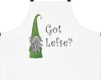 Puede incluir: Delantal blanco con tirantes negros y una ilustración de un gnomo verde. El texto "Got Lefse?" está impreso en el delantal.