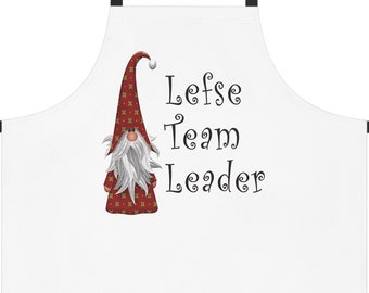 Puede incluir: Delantal blanco con una ilustración de gnomo rojo y dorado y el texto "Lefse Team Leader".