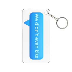 Könnte beinhalten: Ein klarer Acryl-Schlüsselanhänger mit einer silbernen Kette und einem Ring. Der Schlüsselanhänger zeigt eine blaue Textblase mit den weißen Worten "We didn't even kiss", ein humorvolles und modernes Design.