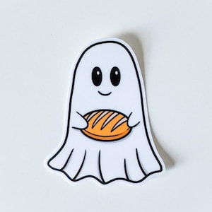 Könnte beinhalten: Ein gestanzter Aufkleber mit einem weißen Cartoon-Geist mit schwarzen Augen und einem kleinen Lächeln. Der Geist hält einen goldbraunen Laib Brot mit dunkelbraunen Schnittlinien auf der Oberfläche. Die Illustration hat einen dicken schwarzen Rand.