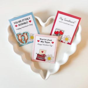 May include: Three Valentine's Day cards with cute illustrations and text. One card says "You Are Otterly Adorable!" with otter stickers. Another says "You're Just My Type." with a typewriter. The third says "Hey Sweetheart!"