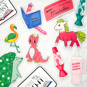 May include: A set of colourful stickers featuring various illustrations, including a bookworm, a dragon, a flamingo, a unicorn, a hedgehog, a lava lamp, a cup, and a reminder that it's okay to make mistakes.