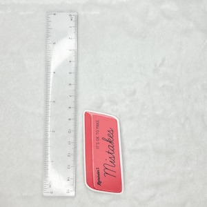 May include: A pink eraser with the text "Reminder: It's OK to make Mistakes" in black cursive writing.