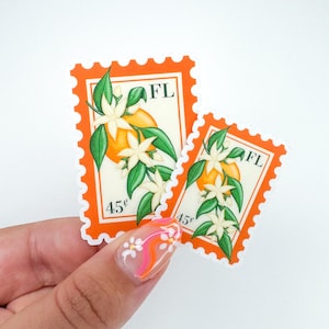 Op de afbeelding: Twee oranje bloesem postzegels met een prijs van 45&cent; en de afkorting "FL" voor Florida. De postzegels tonen een witte bloem met een gele kern en een kleine sinaasappel.