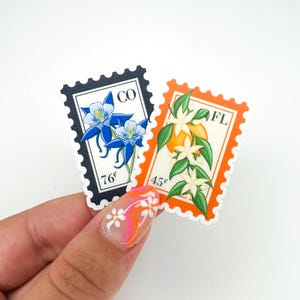 Op de afbeelding: Twee postzegels in vintage stijl met bloemmotieven. De linker postzegel toont een blauwe bloem met de tekst "CO 76&cent;". De rechter postzegel toont een sinaasappelbloesem met de tekst "FL 45&cent;".