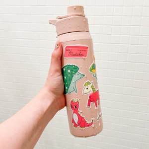 May include: A pink reusable water bottle with a variety of colourful stickers featuring animals and the text "It's OK to Make Mistakes".