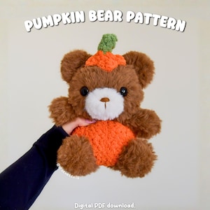 May include: A brown plush bear with a white muzzle, black eyes, and a brown stitched nose. The bear wears an orange pumpkin-shaped body and a small orange pumpkin hat with a green stem. Text reads PUMPKIN BEAR PATTERN and Digital PDF download.