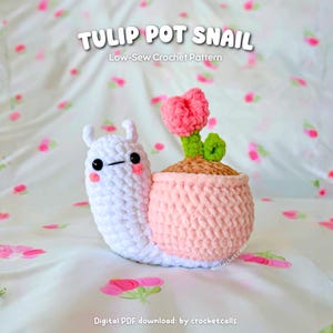 Puede incluir: Un caracol de ganchillo hecho a mano con una maceta rosa en la espalda. El caracol es blanco con ojos negros y mejillas rosas. La maceta es de color rosa claro y contiene un tulipán rosa con hojas verdes. Texto: "TULIP POT SNAIL".