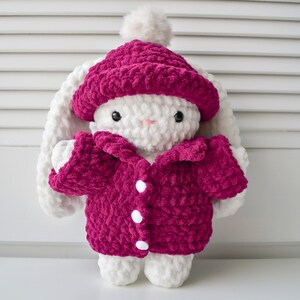 May include: White crocheted bunny wearing a pink crocheted hat and jacket with white buttons.