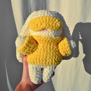 May include: A white crocheted bunny wearing a yellow crocheted sweater and a yellow eye mask.