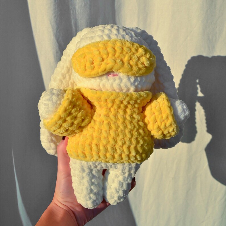 May include: A white crocheted bunny wearing a yellow crocheted sweater and a yellow eye mask.