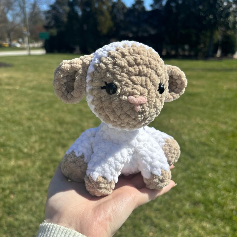 May include: A crocheted plush lamb toy with a white body and brown head. The lamb has black eyes and a pink nose.