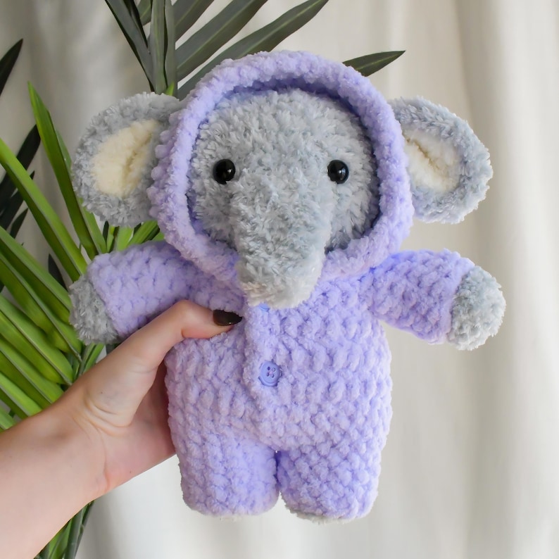 May include: A gray crocheted elephant wearing a lavender hooded onesie with a button closure.