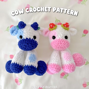 May include: Two plush cow toys made of soft white yarn. The left cow has blue accents and blue berry-shaped horns. The right cow has pink accents and red strawberry-shaped horns. Text reads COW CROCHET PATTERN and Digital PDF download.