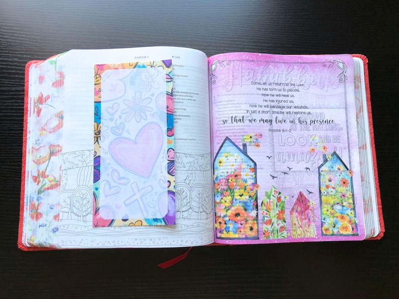 May include: An open Bible with a pink and white floral design on the right page. The left page has a colorful bookmark with a heart and cross design. The text on the right page reads "He has torn us to pieces, now He will bandage our wounds, so that we may live in His presence.  Hosea 6:1-2.  Look and be willing".