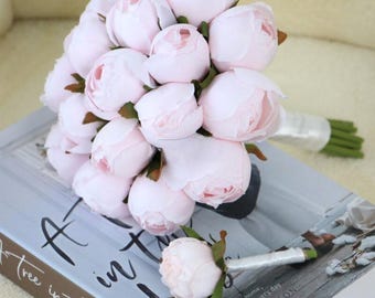 May include: A bouquet of light pink peonies with green stems and a white ribbon, resting on a book titled "A Tree in the House". The book cover has the text "Flowers for your home, special occasions and every day" by Annabelle Hickson.