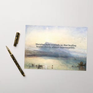 May include: A postcard featuring a serene landscape painting with a lake and mountains under a soft sky. The text "Morning light reminds us that healing begins slowly, almost imperceptibly" is printed on the card. A decorative pen with a floral design is next to the postcard.