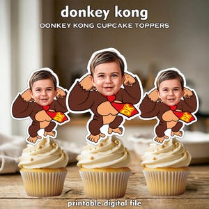 May include: Three cupcakes topped with Donkey Kong-themed toppers featuring a child's face. The toppers are brown and tan with a red tie and a "DK" logo. The cupcakes have white frosting and gold sprinkles. Text at the top reads "donkey kong" and "DONKEY KONG CUPCAKE TOPPERS".