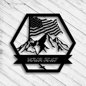 May include: Black metal wall art featuring the American flag waving over a mountain range, set within a hexagonal frame. The words "YOUR TEXT" are displayed on a banner below the mountains, with a flying bird silhouette.