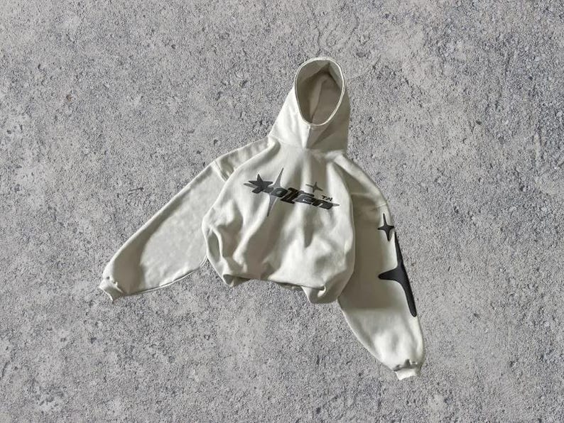 Puede incluir: Una sudadera con capucha gris claro con un gr&aacute;fico negro de una estrella y el texto "XOLVER" en la parte delantera. La sudadera tiene gr&aacute;ficos de estrellas negras en las mangas.