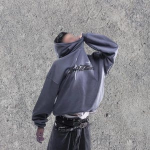 Puede incluir: Una sudadera gris con capucha con un gr&aacute;fico negro que dice "Shattered" en la parte delantera. La sudadera tiene una capucha con cord&oacute;n y un ajuste holgado.