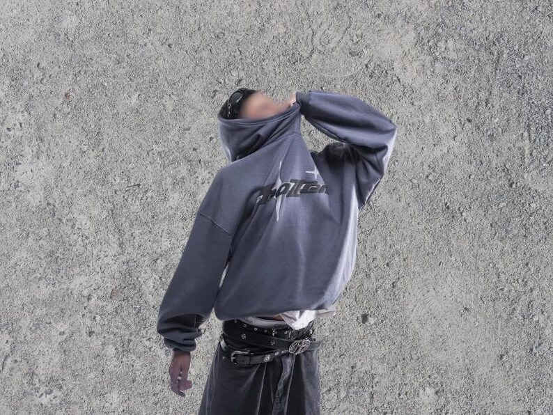 Puede incluir: Una sudadera gris con capucha con un gr&aacute;fico negro que dice "Shattered" en la parte delantera. La sudadera tiene una capucha con cord&oacute;n y un ajuste holgado.