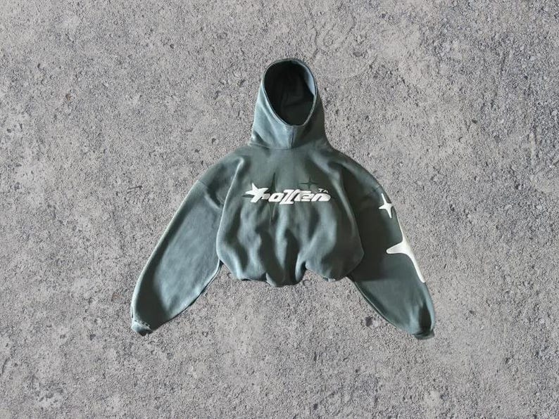 Puede incluir: Una sudadera con capucha verde recortada con una estrella blanca y el texto "Fallen" en la parte delantera. La sudadera tiene dise&ntilde;os de estrellas blancas en las mangas.
