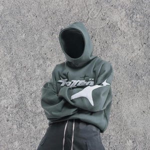 Puede incluir: Una sudadera con capucha de color verde oscuro con un dise&ntilde;o gr&aacute;fico blanco que dice "Rotten" con una estrella a cada lado de la palabra. La capucha est&aacute; levantada y la sudadera est&aacute; doblada en las mangas.