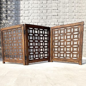 May include: A three-panel room divider made of dark brown wood with a geometric pattern cut out. The divider is made of three panels that are hinged together.