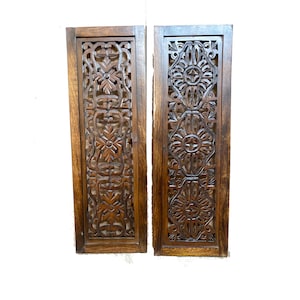 Peut inclure: Deux panneaux muraux en bois brun avec des motifs floraux sculptés complexes. Les panneaux sont rectangulaires et ont une finition brun foncé.