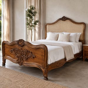 Könnte beinhalten: Ein Holzbettgestell mit einem kunstvoll handgeschnitzten Kopf- und Fußteil mit detaillierten Blumenverzierungen. Das Kopfteil enthält ein natürliches Geflecht aus Rattan. Das Bett ist mit weißer Bettwäsche und einer hellbeigen Decke bezogen.