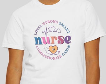 以下が含まれることがあります： 白いTシャツ。カラフルなグラフィックデザインで、円形のデザインに「nurse」と書かれています。デザインには心臓、心拍ライン、そして「忠実、強い、賢い、思いやり、思いやり」という言葉が含まれています。