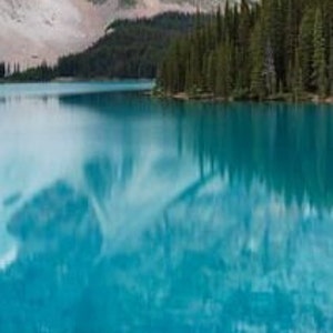 May include: A mountain lake with a reflection of the surrounding mountains and trees in the water. The water is a vibrant blue color.