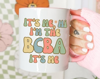 May include: White ceramic mug with a colorful retro design that says "It's me, hi I'm the BCBA It's me".
