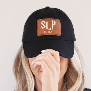 May include: Black baseball cap with a brown leather patch that says "SLP Est. 2024" in white lettering.